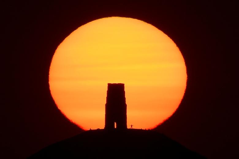 A person views the sun rise from beside the remains of Saint Michael's Church on top of Glastonbury Tor, as the hottest day so far of the summer in Britain is predicted, in Glastonbury, southwest Britain. REUTERS/Toby Melville    